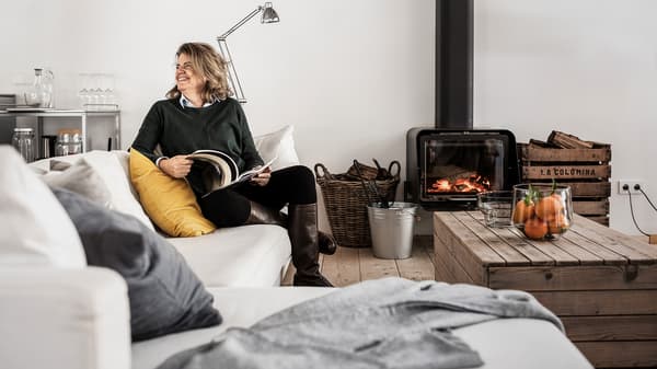 Lachende vrouw zit op de bank in een woonkamer en leest een tijdschrift.