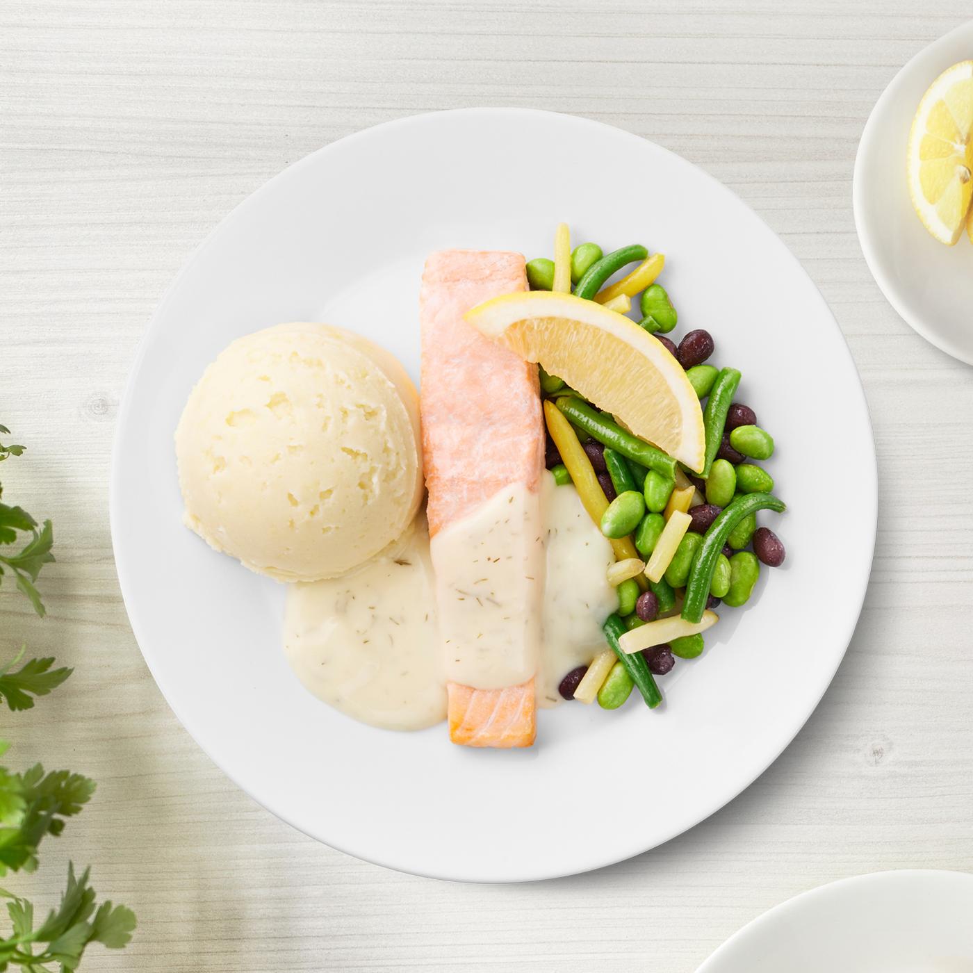 Lachsfilet mit Fisolen, Bohnen, Kartoffelpüree mit Dillsauce auf einem Teller präsentiert.