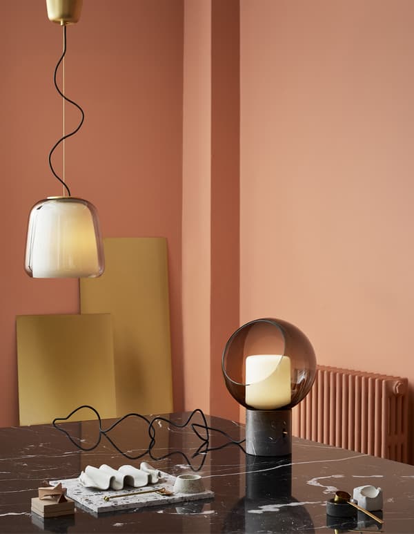 Lampada a sospensione in vetro e lampada da tavolo sferica EVEDAL su un tavolo in marmo nero, in una stanza  rosa.
