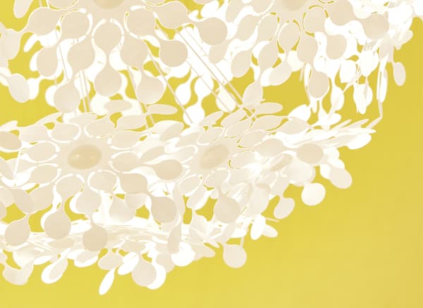 Lampada bianca con motivo floreale perforato su sfondo giallo.