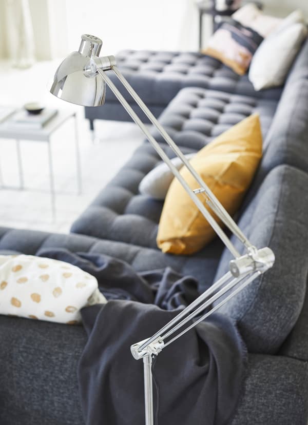 Lampadaire IKEA ANTIFONI nickelé au-dessus d’un canapé LANDSKRONA gris foncé.
