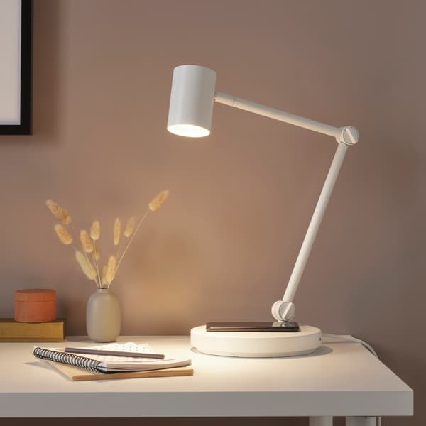 Lámpara de mesa NYMÅNE blanca que es también cargador inalámbrico de celular sobre una mesa blanca.
