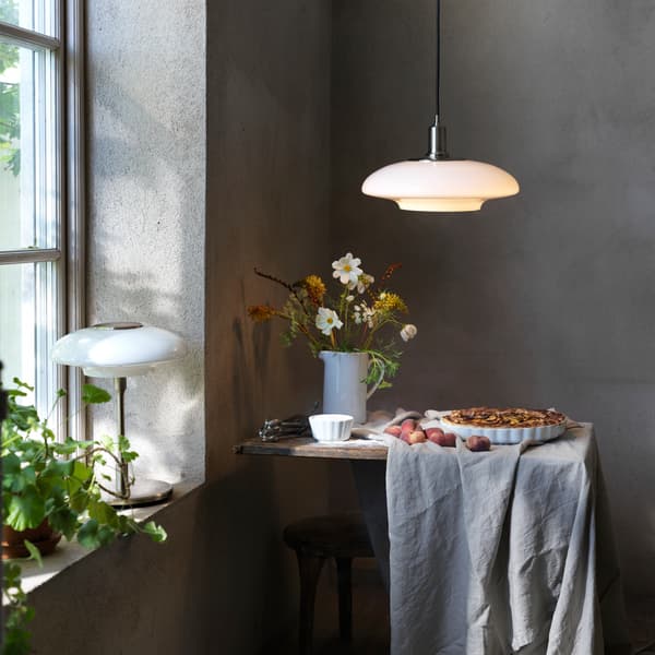 Lámpara de mesa TÄLLBYN sobre un alféizar y lámpara de techo TÄLLBYN colgada sobre una mesa con una tarta y flores.