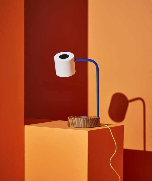 Lampe de bureau à socle marron, bras bleu et abat-jour blanc, sur une marche orange.