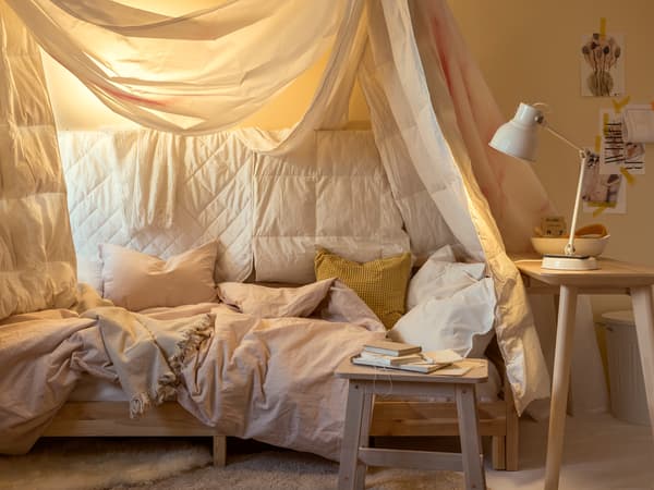 Lampe de travail HEKTAR blanche et lit drapé de linge de lit varié dans les tons de blanc, de jaune et de rose. 