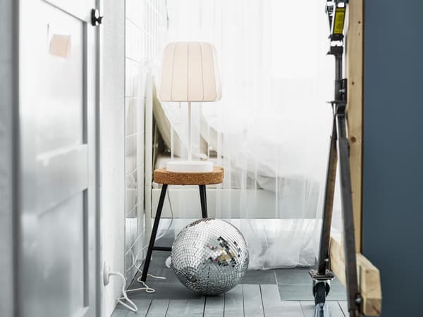 Lampe posée sur un tabouret en liège à côté d’un lit garni de linge blanc, avec boule disco à l’avant-plan. Quelle est votre chambre à coucher idéale?