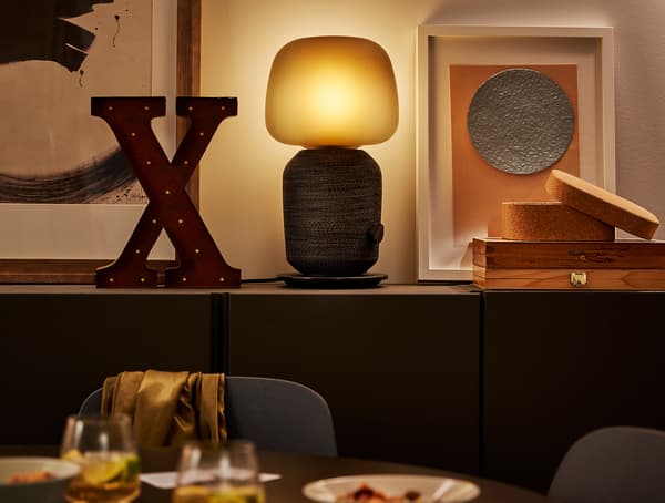 Lampe SYMFONISK avec enceinte Wi-Fi et diverses accessoires de décoration sur un meuble de salle à manger.
