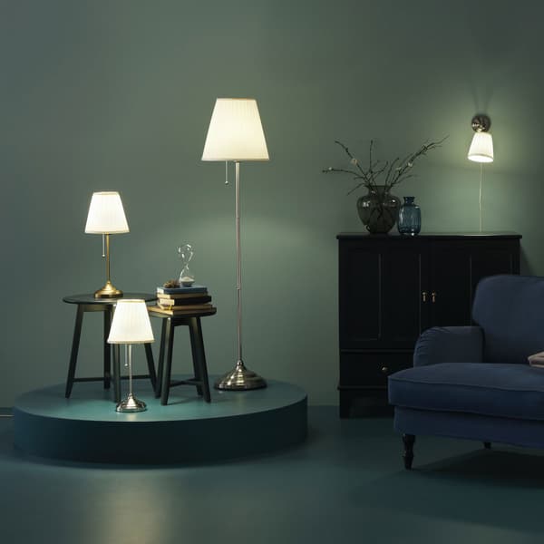 Lampes ARSTID dans une décor vert foncé, posé sur le sol et sur des meubles foncés 