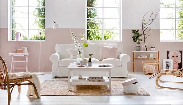 Landelijk interieur met witte bank, rotan stoelen, woonaccessoires en een lichtroze lambrisering op de wand