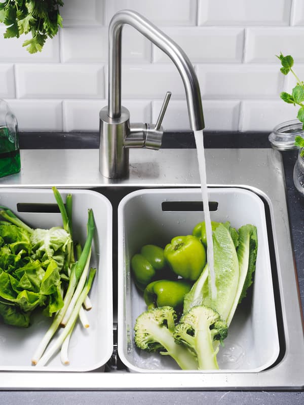LÅNGUDDEN mosogató BOSJÖN keverőcsappal és két világosszürke GRUNDVATTNET mosogatótál, amelyben zöldségeket öblítenek le.
