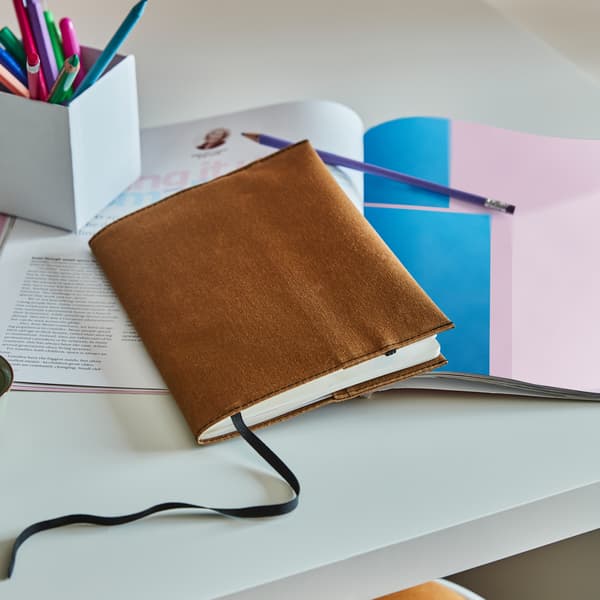 브라운 색상의 LANKMOJ 랑크모이 노트커버로 보호된 노트가 다른 노트, 펜, 연필과 함께 테이블에 놓여져 있는 모습
