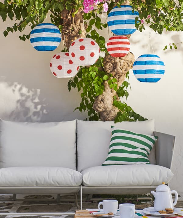 Lanternes colorées suspendues à un arbre au-dessus d’un canapé d’extérieur.