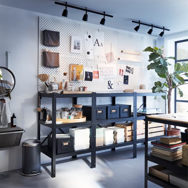 Large black shelving unit, white pegboards with accessories on the wall above and two black ceiling tracks with spotlights.