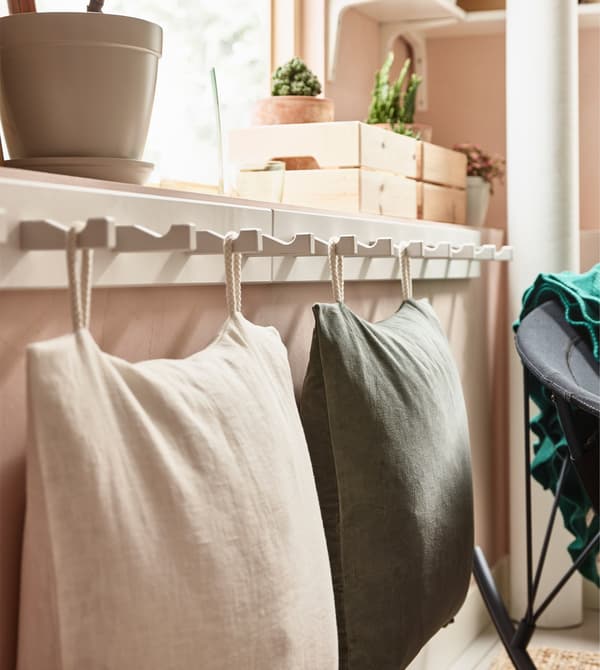 Large soft cushions for floor seating are stored by hanging them on a white KUBBIS rack with hooks.