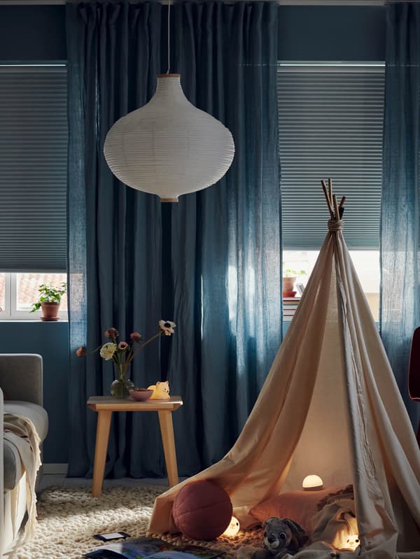 Látkový stan v obývacej izbe s oknami, na ktorých sú stiahnuté rolety PRAKTLYSING.