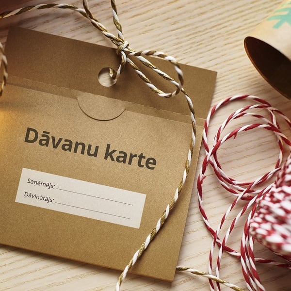 Latvian gift card envelope with decorative twine on wooden table, labeled 'Dāvanu karte' for recipient and giver details.