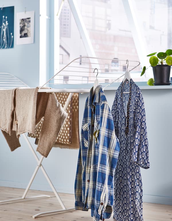Laundry hangs on a drying rack in a white room.