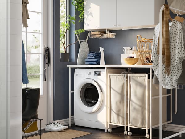 Lavanderia con pareti blu e una combinazione di mobili ENHET bianchi, una lavatrice, uno stand appendiabiti e sacchi per il bucato con rotelle - IKEA.