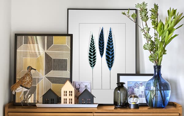 Layered pictures, ornaments, and vases on a natural wood cabinet in a white room.