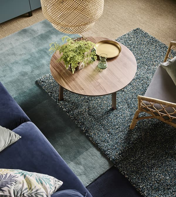 Layered rugs in shades of green under a round, wood coffee table in a living room.