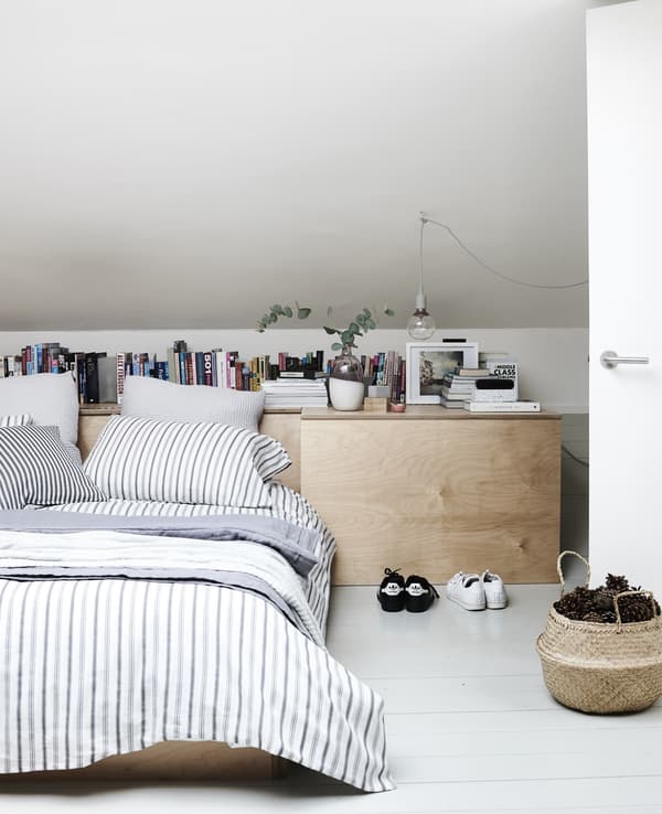 Layers of striped bed textiles on a low bed for two in a minimal bedroom with a wood chest of drawers.