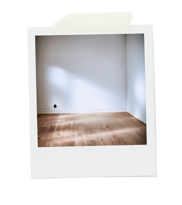 Le coin d’une pièce vide baignée de soleil avec des murs nus et blancs et un plancher en bois constitué de larges planches non traitées.