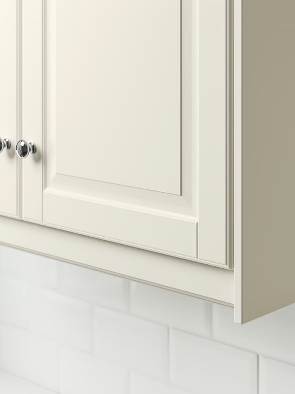Le coin inférieur d’une armoire blanc cassé avec son bandeau-décor blanc cassé.