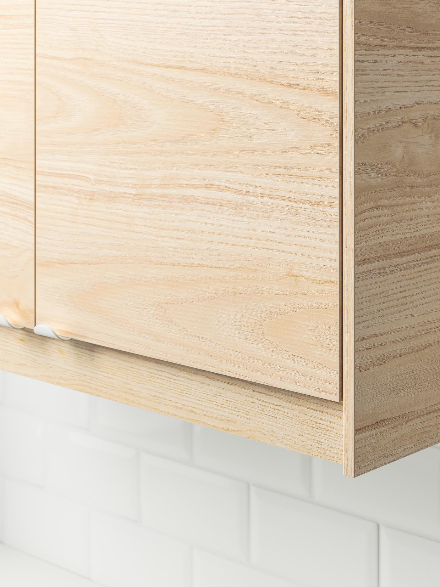 Le coin inférieur d’une armoire murale de cuisine IKEA SEKTION avec une porte ASKERSUND à effet frêne clair.