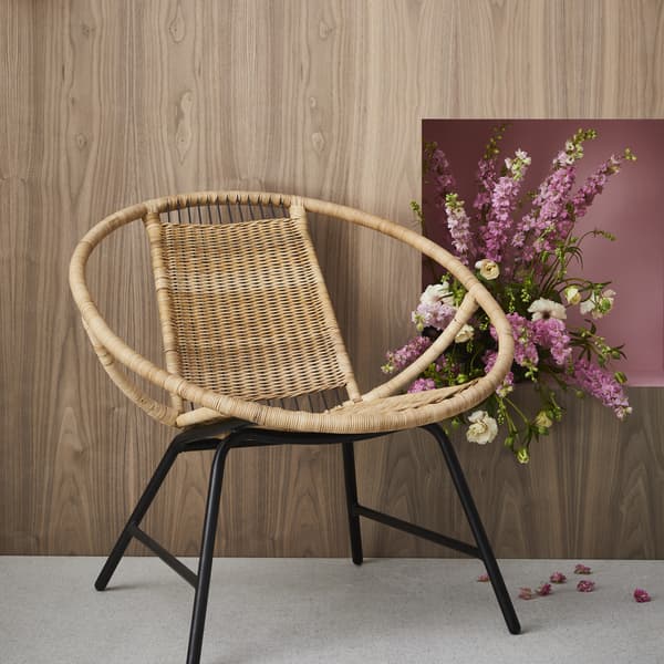 Le fauteuil en rotin GAGNET, à côté de fleurs roses.
