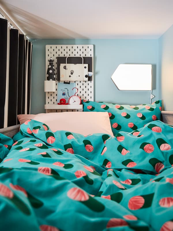 Le linge de lit GRACIÖS crée un paysage textile évocateur dans un petit nid constitué par un lit mezzanine, des rideaux, une lampe et un panneau perforé servant de table de nuit.