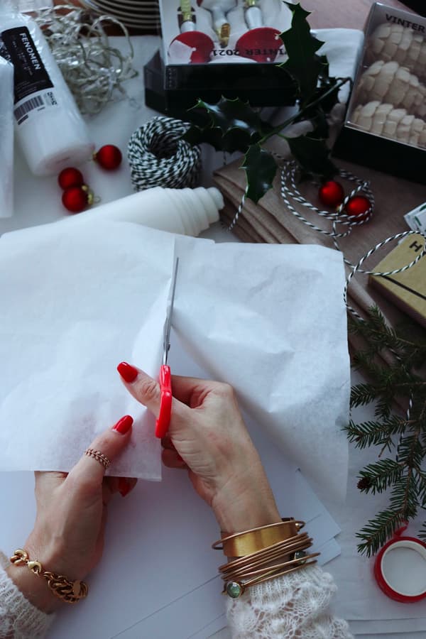 .Le mani di una donna tagliano un pezzo di carta velina bianca con le forbici.