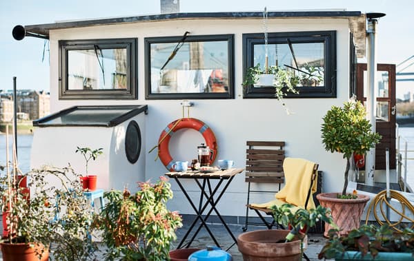 Le pont d'une péniche avec des plantes vertes, table et chaises.