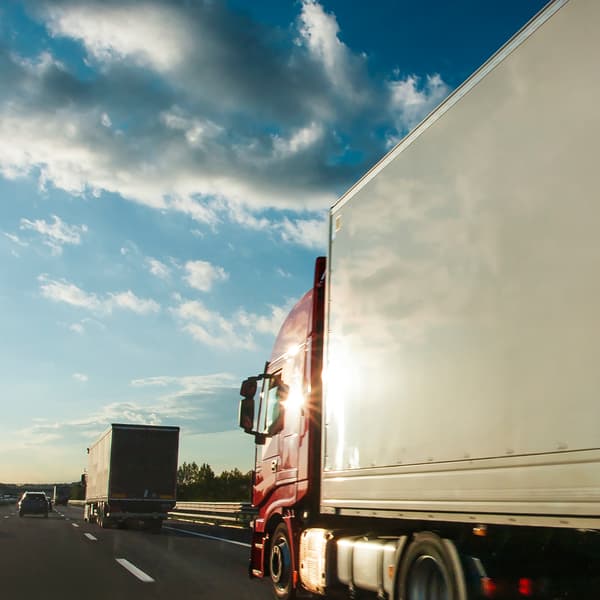 Le soleil du soir se reflète sur la cabine rouge d’un semi-remorque roulant sur l’autoroute derrière un autre camion.