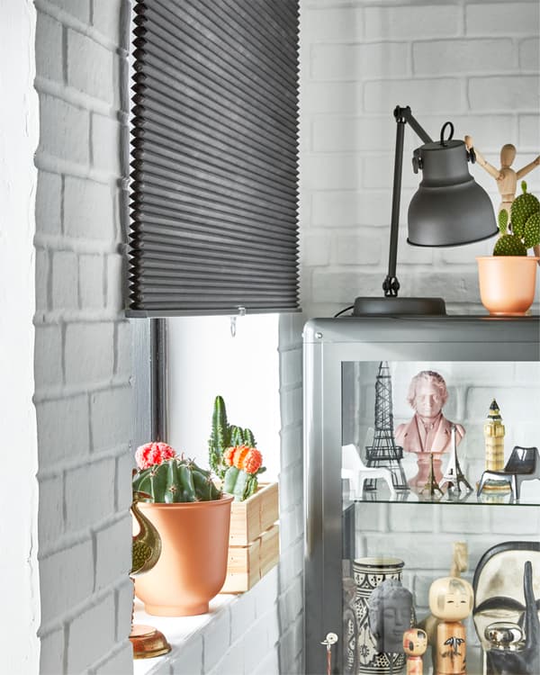 Le store alvéolaire obscurcissant gris IKEA HOPPVALS couvre la moitié de la fenêtre et permet d’assombrir la pièce de jour comme de nuit.