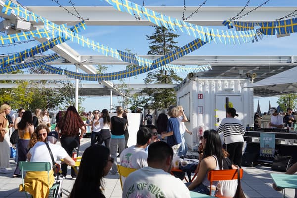 Lebendiger IKEA-Dachterrassen-Event mit vielen Besuchern, bunten Stühlen und schwedischen Flaggen als Dekoration. Gäste genießen das sonnige Wetter, Musik und kulinarische Angebote im Freien.