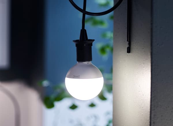 LED lightbulb hanging from a black cord against a dark blue wall.