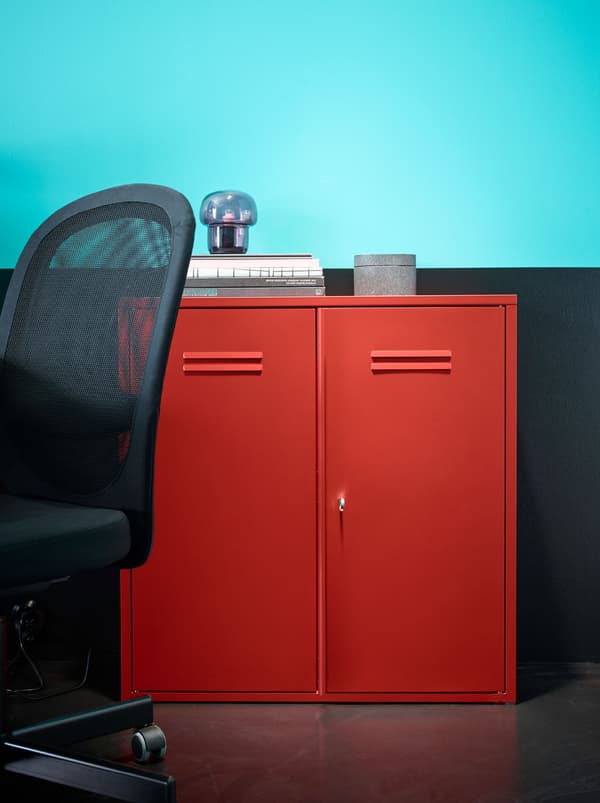 L’élément à portes IVAR rouge devant un mur turquoise et noir, à côté d’une chaise FLINTAN noire.
