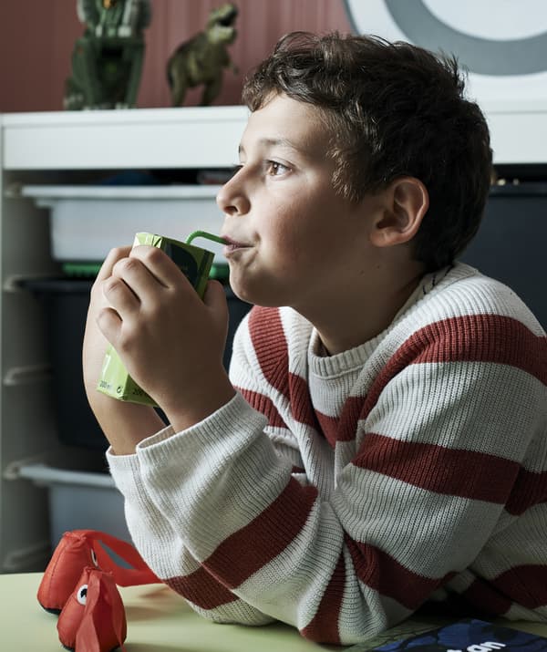 Leo ลูกชายของ Amélie ดื่มจากกล่องกระดาษโดยมีของเล่นล้อมรอบตัวเขา