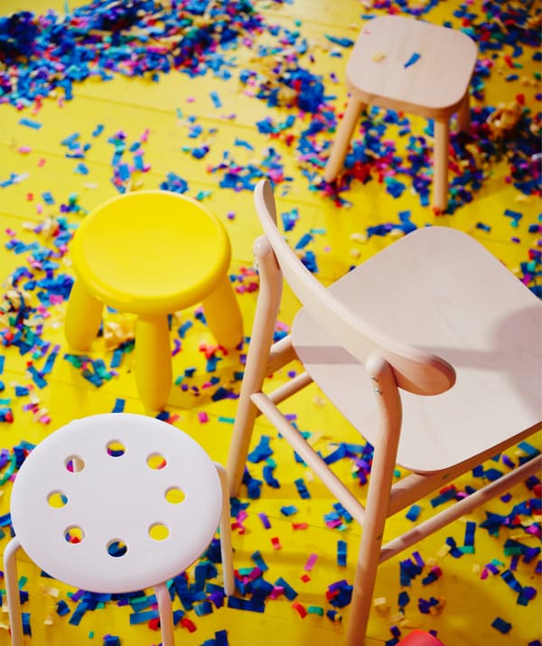 Les chaises MAMMUT et MARIUS en plastique et la chaise RÖNNINGE en bouleau prennent place sur un sol jaune couvert de confettis.