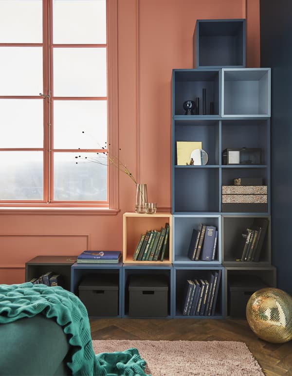 Les éléments modulaires comme EKET de chez IKEA permettent de construire facilement des rangements muraux sur mesure, comme celui-ci en L inversé, dans un coin. Les teintes bleues et grises uniformisent le look tout en titillant le regard. Une touche d’orange apporte un côté ludique à l’ensemble.