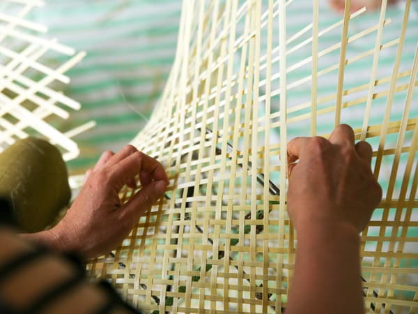 Les mains d’un tisserand assis, tissant à la main un treillis à partir de longs et fins brins de bambou.