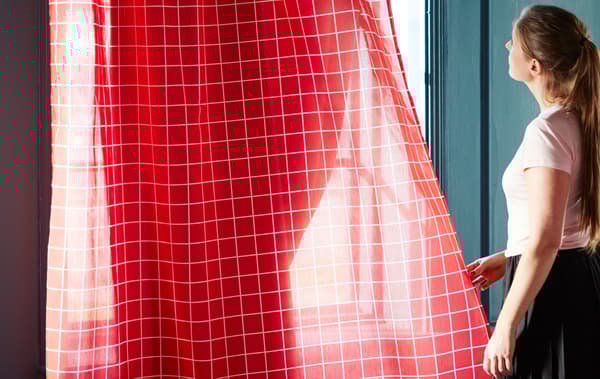 Les voilages IKEA ROSALILL aux lignes blanches sur fond rouge laissant filtrer quelques rayons de soleil.