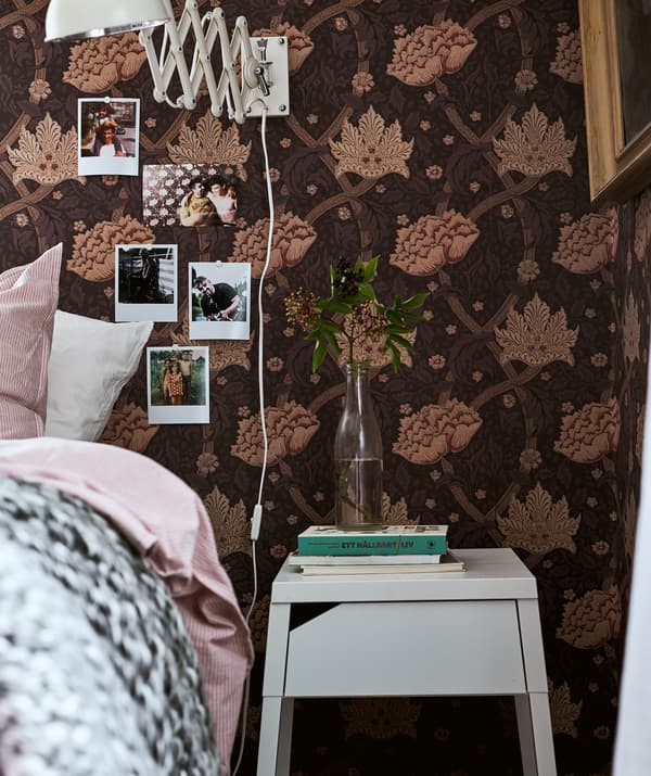 Letto con biancheria rosa accanto a un comodino bianco con libri e un rametto in un vaso, Polaroid appese al muro.