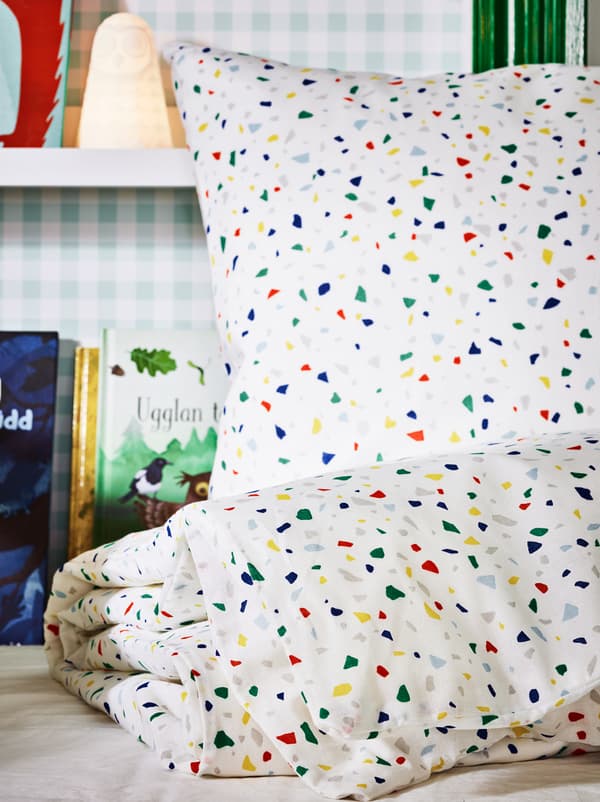 Letto con copripiumino e federa MÖJLIGHET, lampada a LED SOLBO e, sulla parete, mensole per quadri con libri.