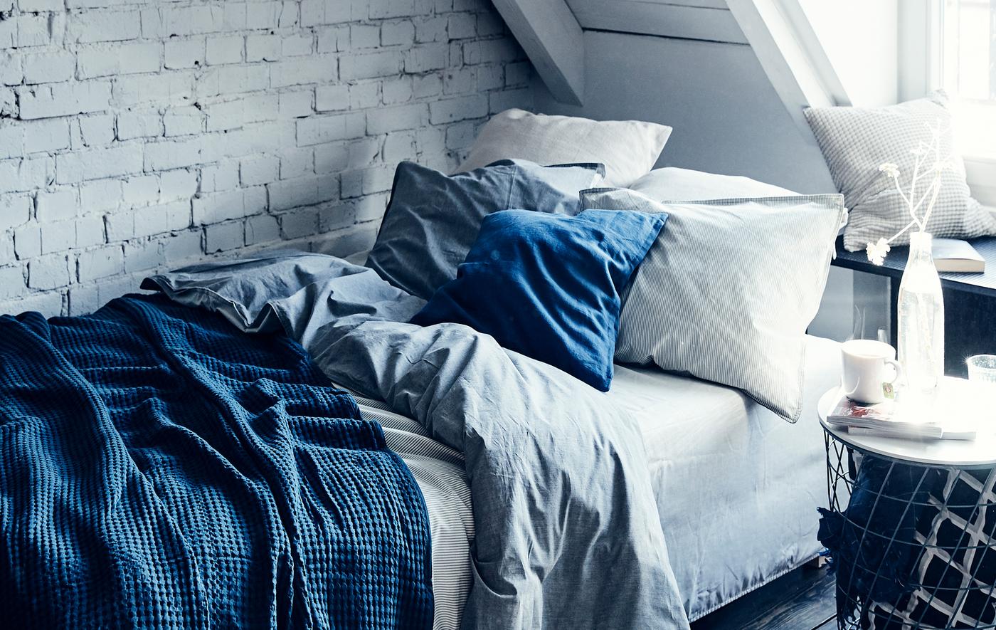 Letto con cuscini e biancheria blu e bianca sullo sfondo di una parete di mattoni dipinta di bianco - IKEA
