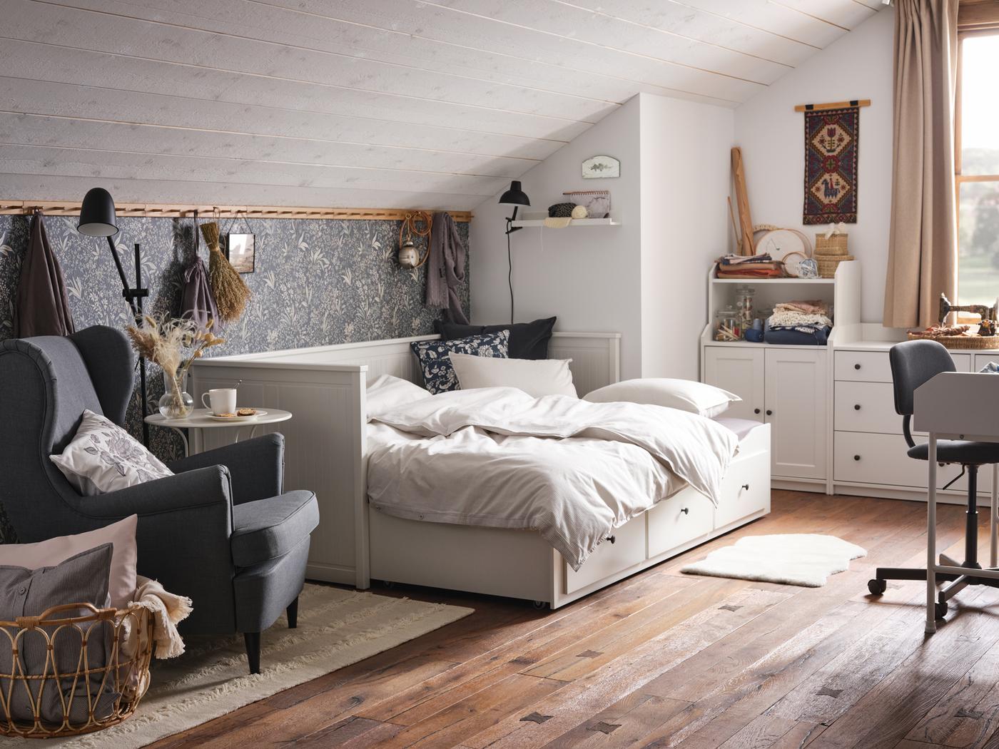 Letto divano con 3 cassetti HEMNES bianco in una stanza in stile country con un pavimento in legno. Accanto, una poltrona STRANDMON - IKEA.