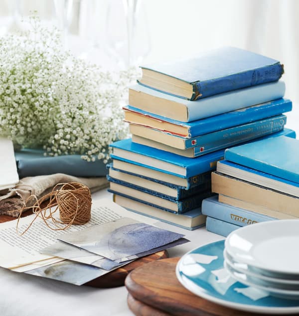 Libros azuis, flores veo de noiva e pratos esperando no centro da mesa a ser colocados.