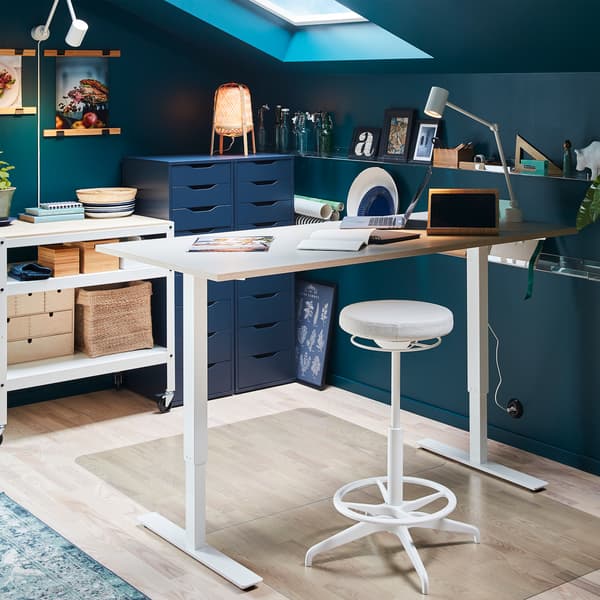 LIDKULLEN sit/stand support stands by a raised sit/stand desk. Transparent floor protectors spare the floor from scratches.