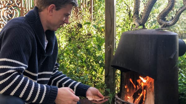 Lien vers « La vie à la maison en des temps incertains - Partie 3 : des expériences partagées » - image d'un homme portant un chandail bleu marine avec des rayures blanches, préparant un feu dans un foyer.