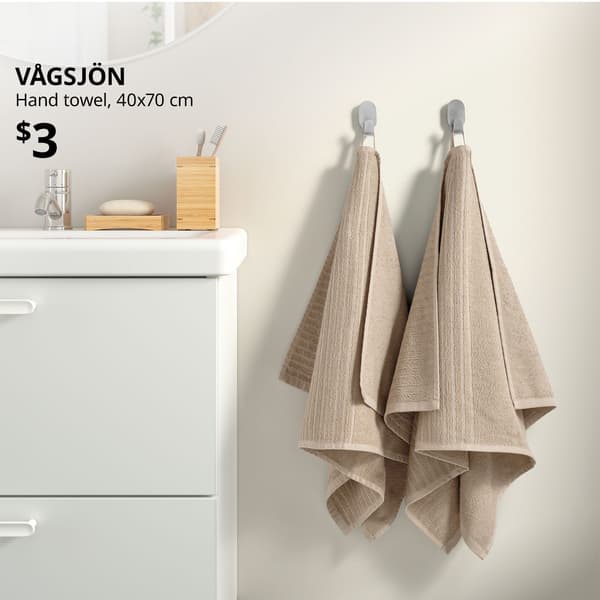 Light beige VÅGSJÖN hand towel hung on stainless steel BROGRUND hook in bathroom setting next to .